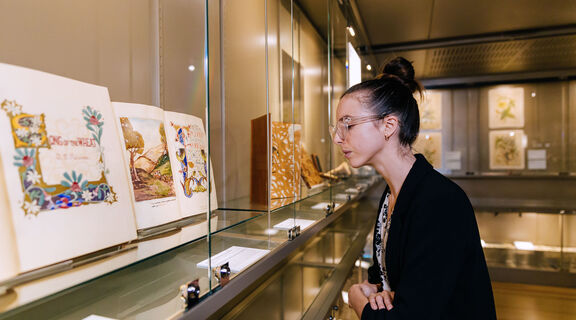 Woman looking at old illustrated book behind a glass cabinet.