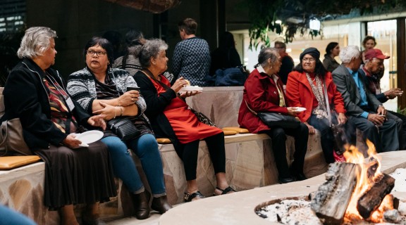 Visitors chatting and eating while gathered around a lit fire in the Talking Circle. 