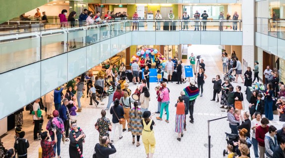 A crowd of people, some playing instruments, on the ground level of State Library. 