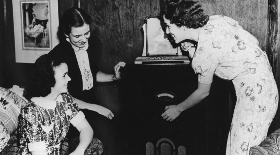 Three ladies gathered around an old fashioned radio