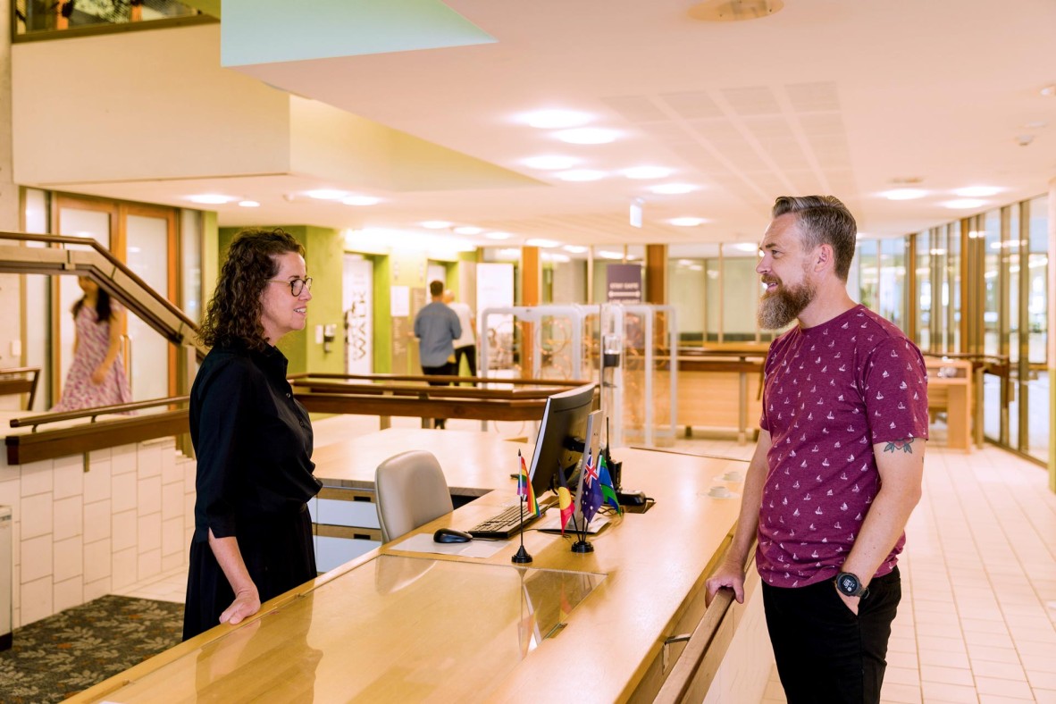 Man talking to State Library staff member standing behind reception desk. 